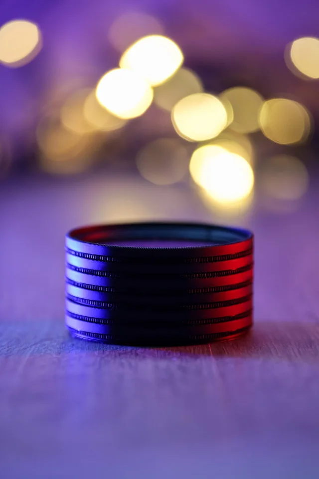 紫の背景と暖かな金色の玉ボケを背に、青と赤の光を受けるレンズフィルター